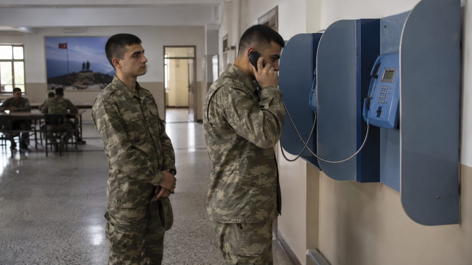 Kışladaki ankesörlü telefondan ailesiyle görüşen ve arkasında sırasını bekleyen askerlik yükümlüsü